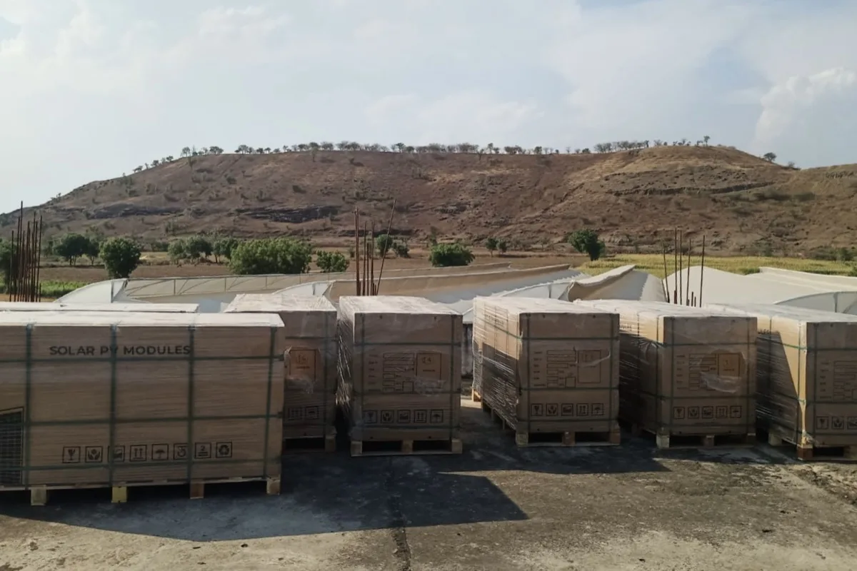 Stacked crates of solar PV modules on delivery day, with a hill behind